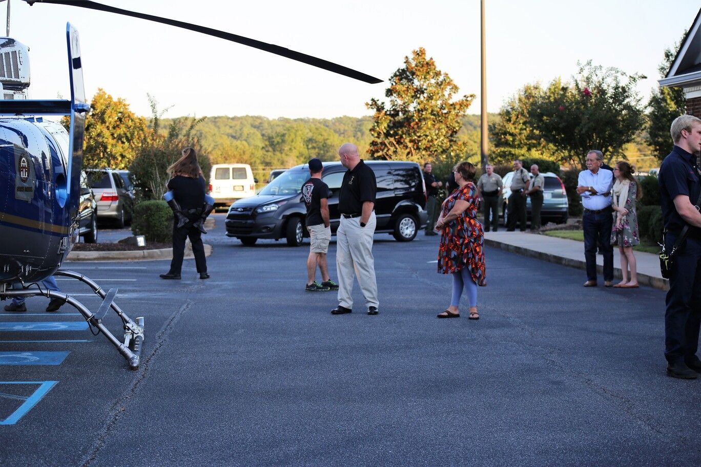 People gathered near a blue helicopter in a parking lot at dusk