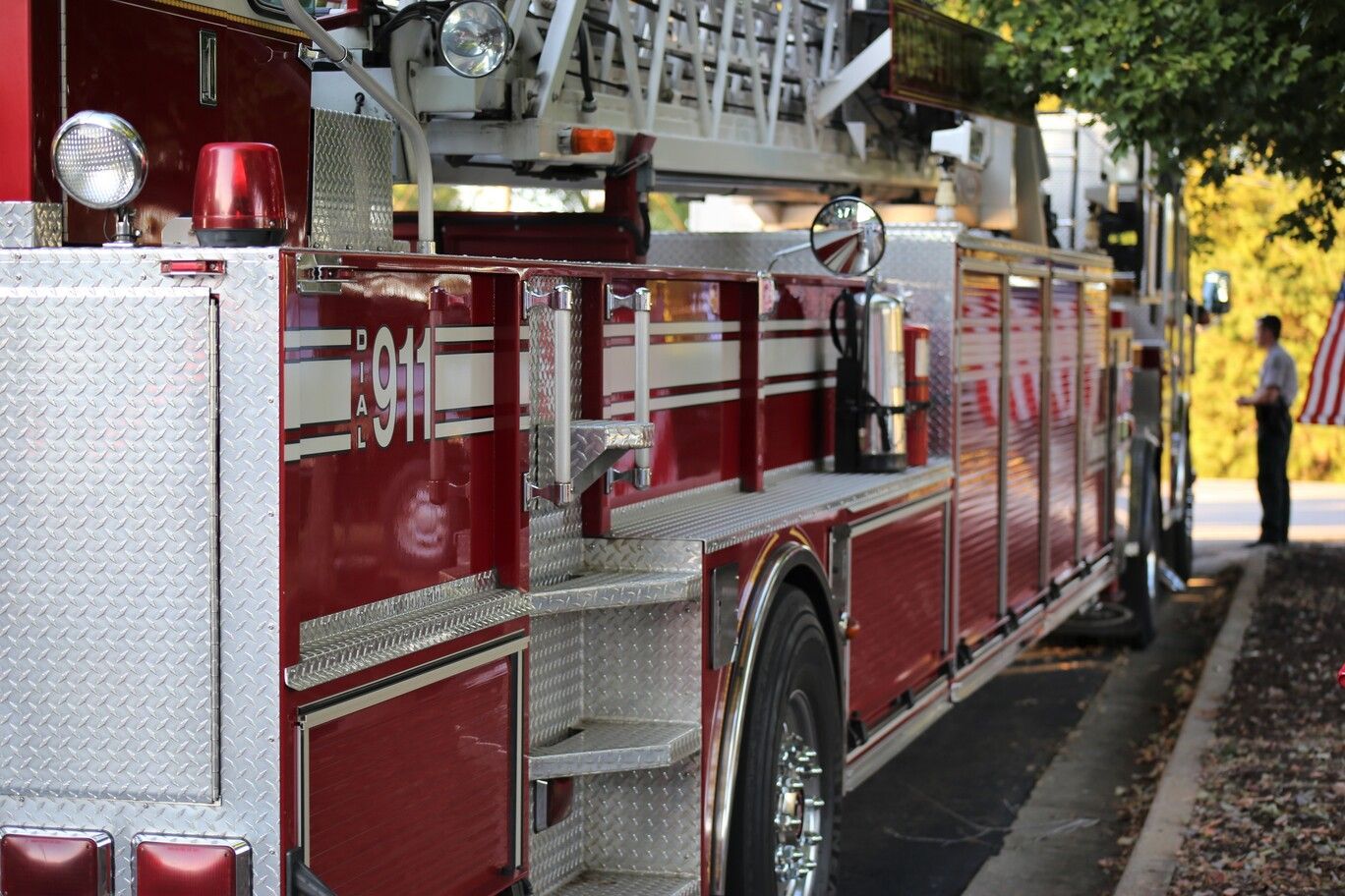 Red fire truck parked curbside with lights and silver ladder, seen from the side