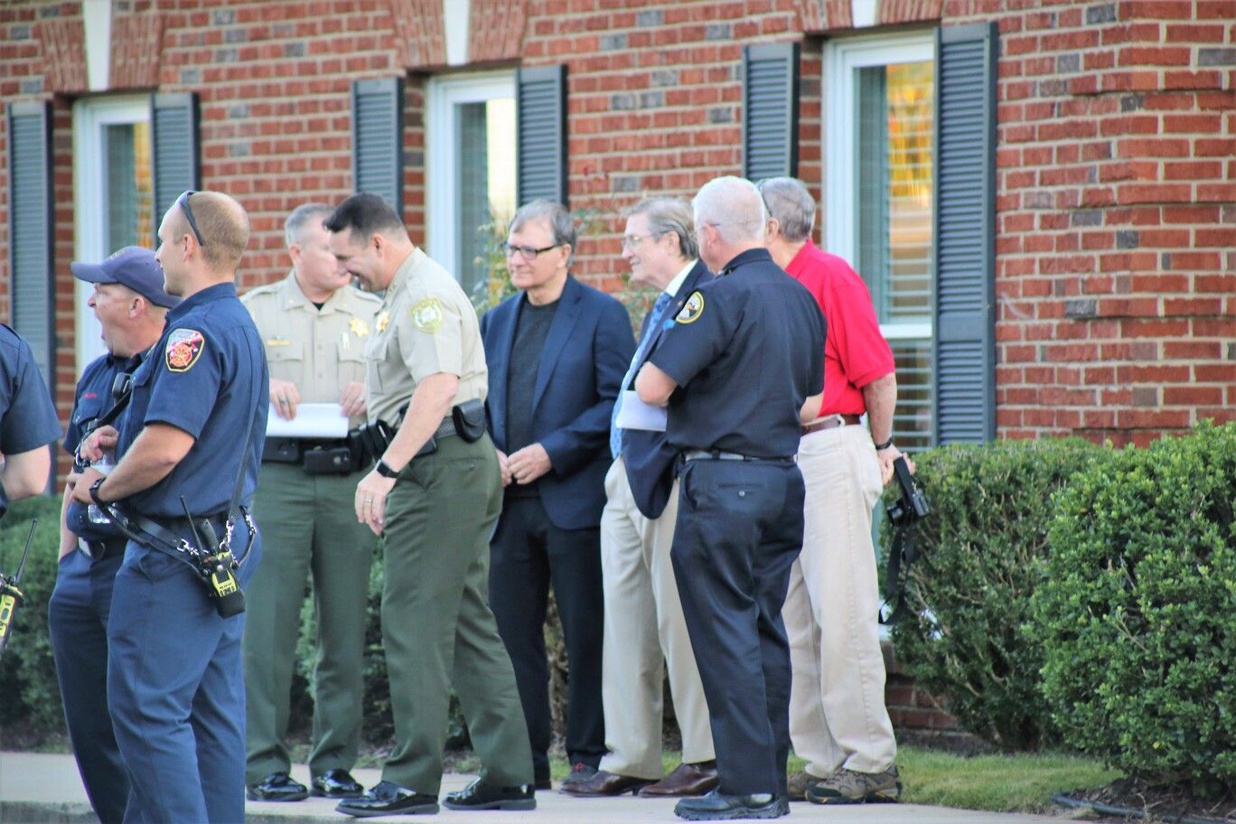 Group of police officers standing outside a brick building near a hedge