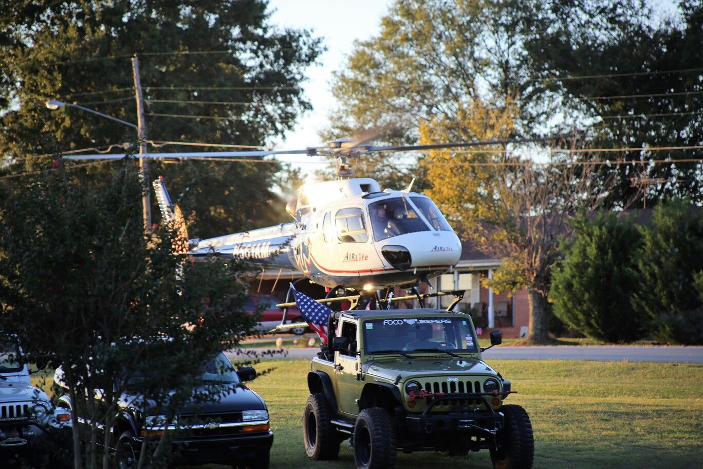 White helicopter on a Jeep in a suburban street, with trees and parked cars nearby.