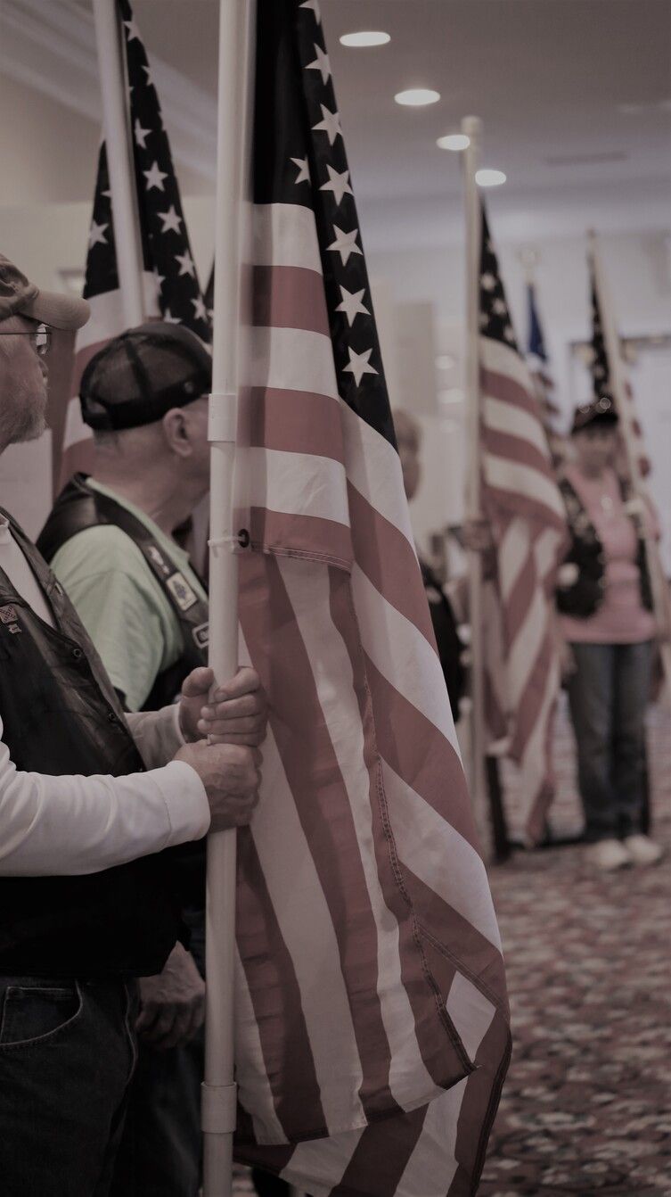 People holding American flags in an indoor hallway or lobby, seen in a row from the side.