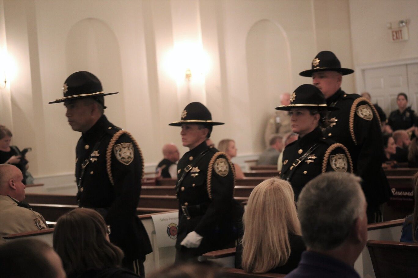 Uniformed officers walking in a church aisle during a ceremony, with seated attendees in the pews.
