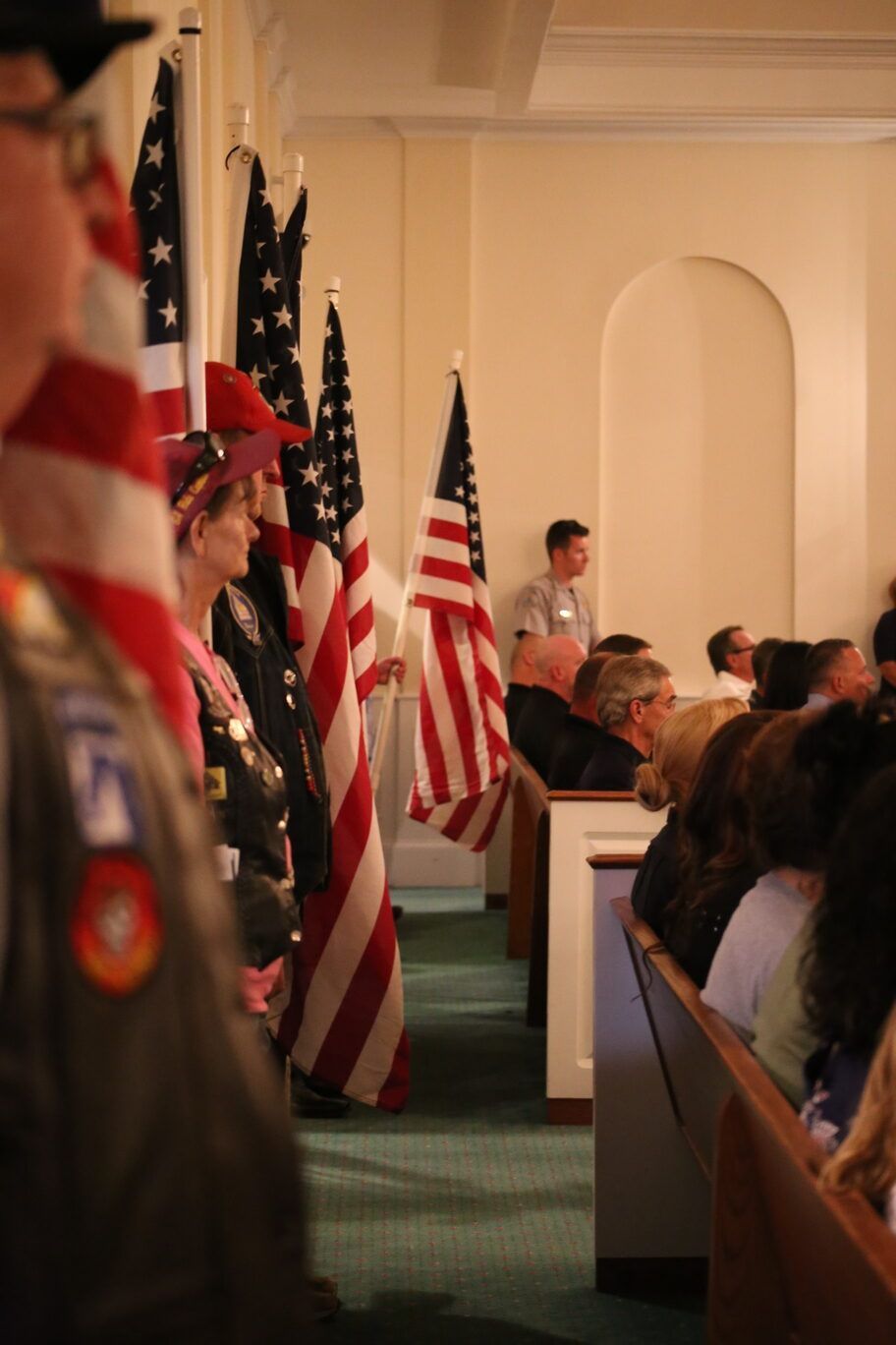 Flags lining an indoor ceremony aisle with people seated in a church-like hall