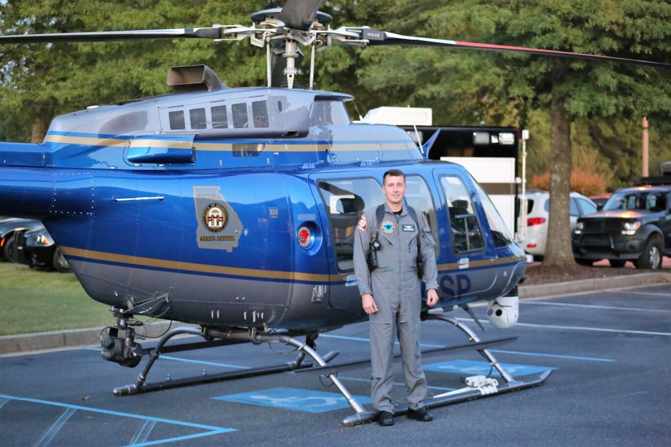 Uniformed officer standing beside a blue police helicopter on a parking lot.
