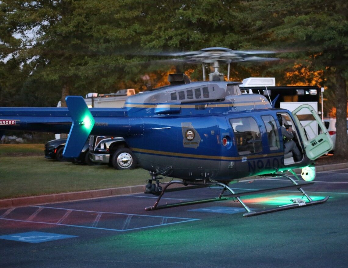 Blue helicopter parked on a road at dusk, with rotors still and lights glowing green and red