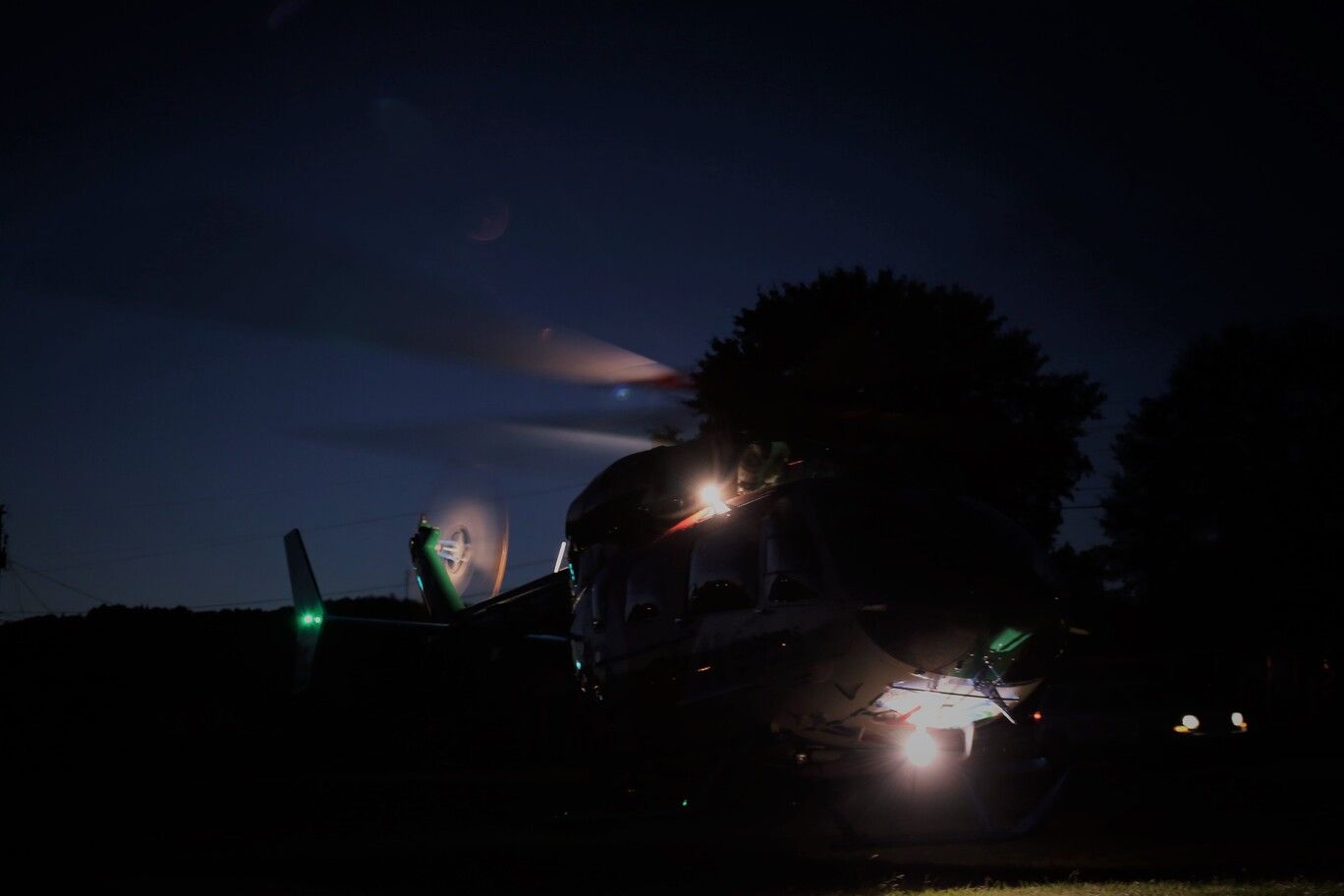 Dark night sky over a military jet on the ground, with bright lights and a glowing cloud behind it.