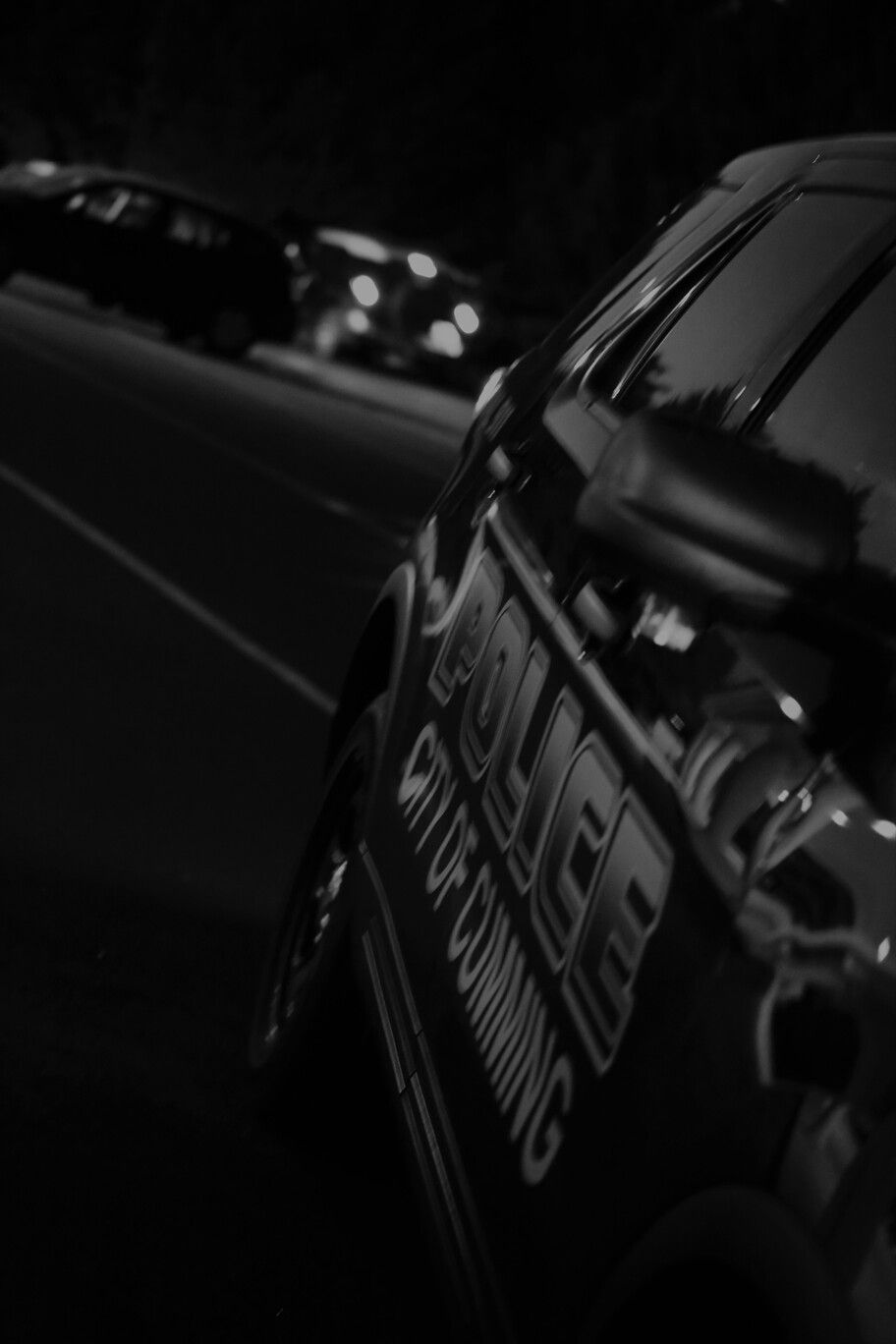 Black-and-white close-up of a race car on a dark track at night, with another car blurred in the background