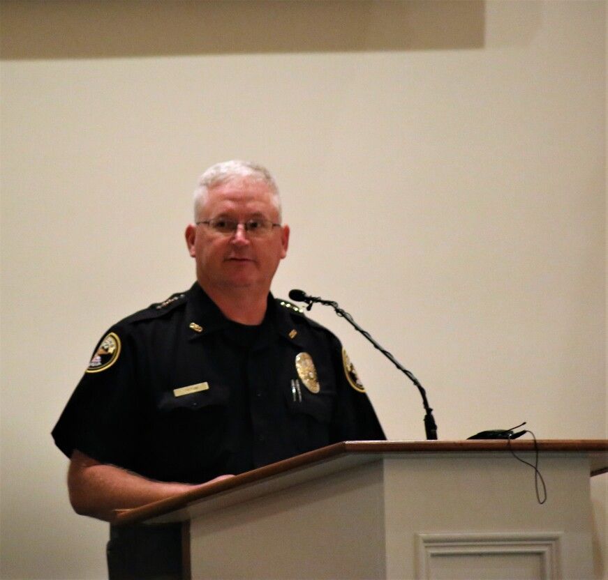 Police officer speaking at a podium with a microphone in a plain indoor room