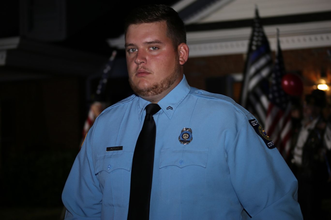 Uniformed officer in a light blue shirt and black tie standing indoors at a formal event.