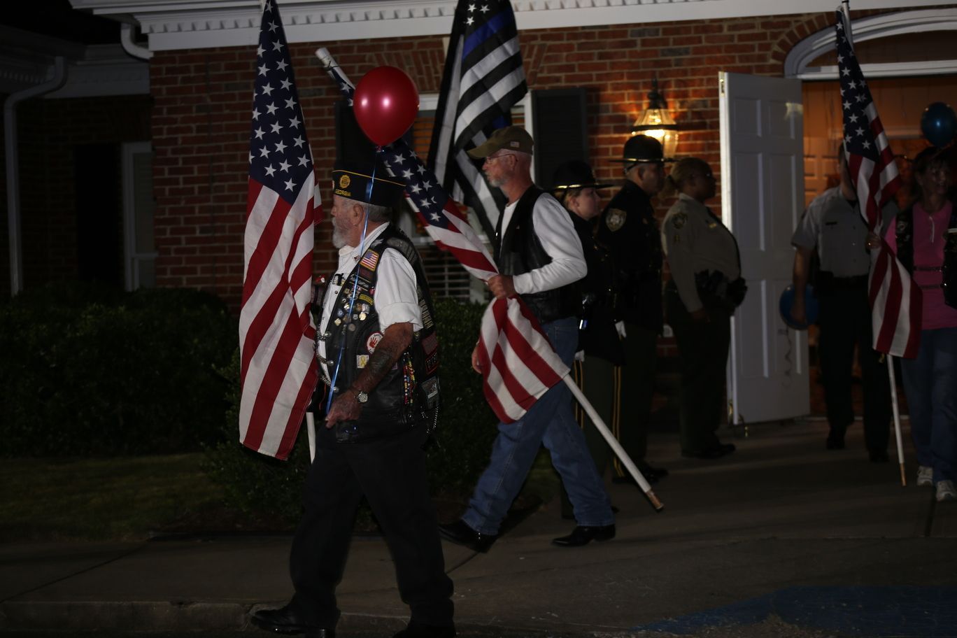People walking at night with American flags and a red balloon outside a brick building