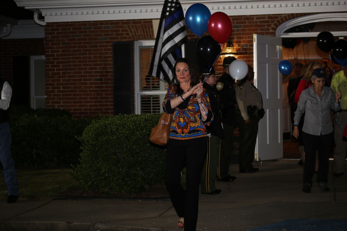 Woman holding balloons walks outside at night near a brick building entrance