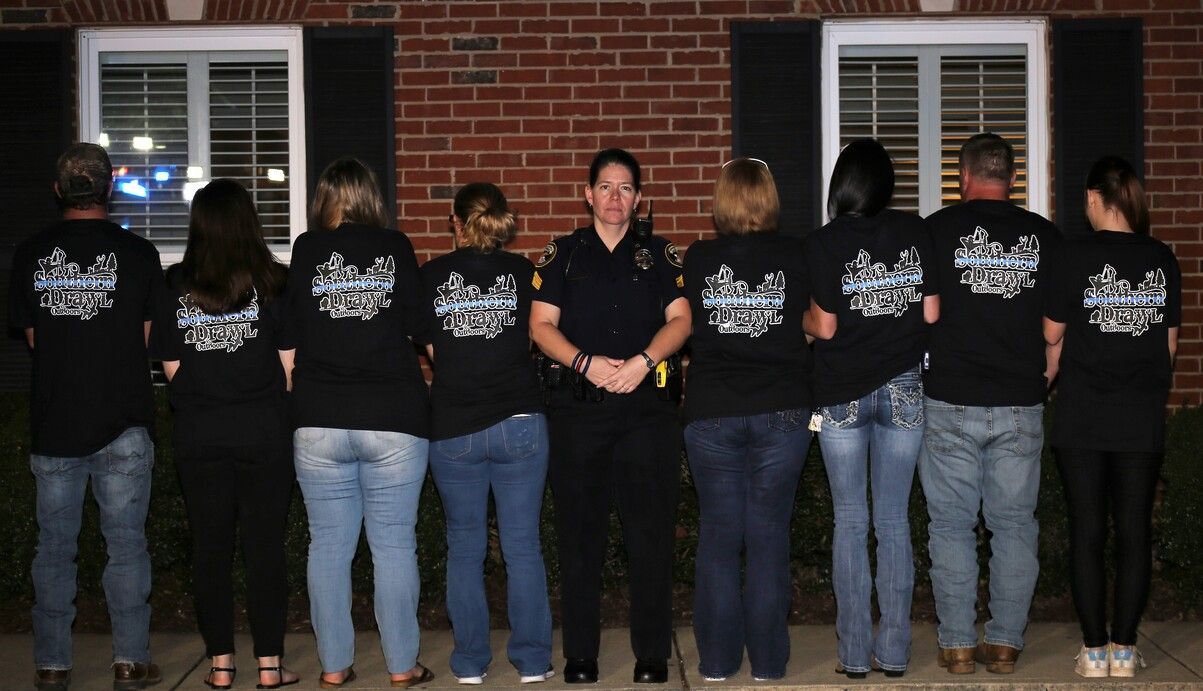 Group in black shirts stands with backs turned in front of a brick building at night