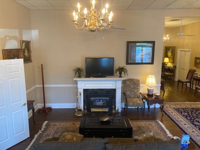 Living room with fireplace, chandelier, TV, and chairs, viewed through an open doorway