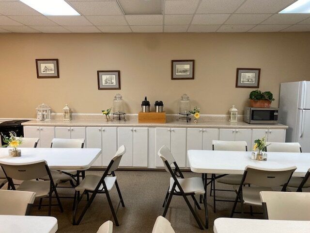Quiet dining area with white tables, folding chairs, and a buffet counter along the back wall