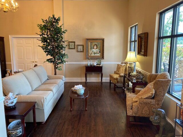Elegant living room with cream sofa, patterned armchairs, wood floor, and large windows with greenery view
