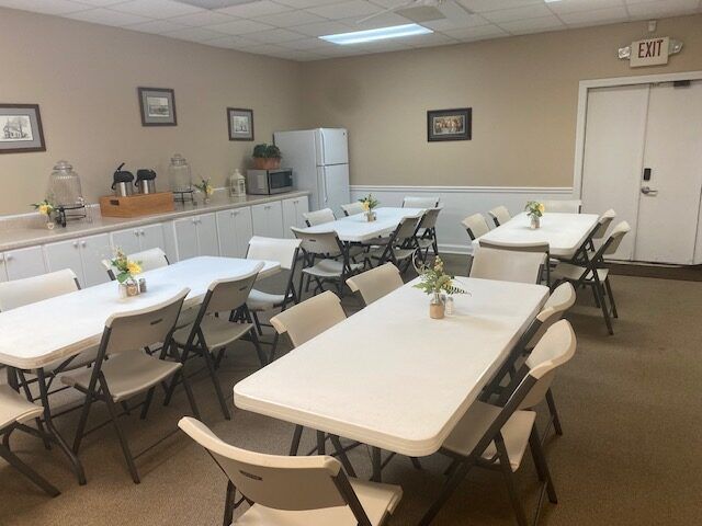 Indoor banquet room with white-clothed tables, folding chairs, and a side buffet table