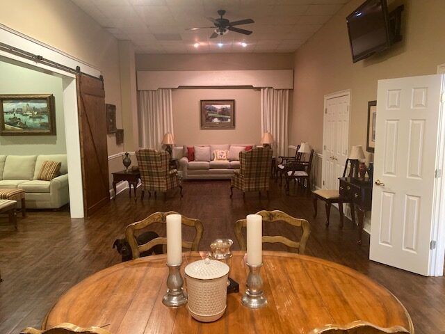 Warm living room with hardwood floors, dining table in foreground, sofa and chairs at the back, TV on wall.