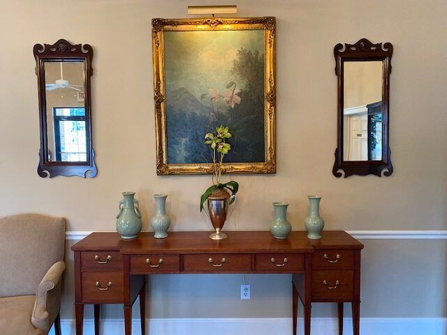 Wooden console table with vases beneath framed artwork, flanked by two wall mirrors in a living room