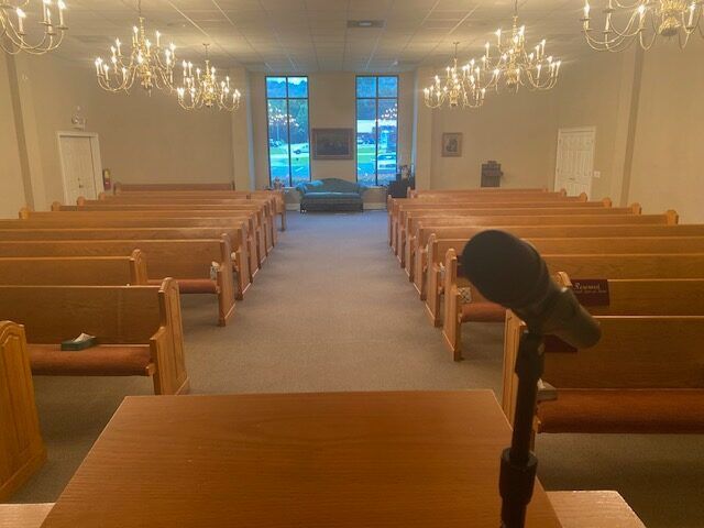 Empty church sanctuary with wooden pews, chandeliers, stained-glass windows, and a microphone in the foreground