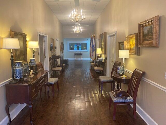 Elegant hallway with polished wood floors, lamps, and framed paintings leading to a distant room