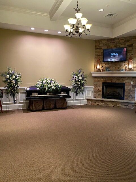 Empty event hall with beige carpet, floral arrangements, chandelier, and stone fireplace with TV above it