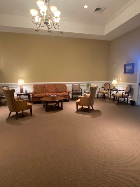 Quiet lounge with beige walls, chandelier, and upholstered chairs around low tables on carpeted floor