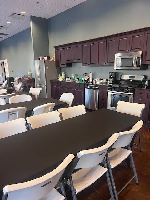 Break room with tables, folding chairs, kitchenette cabinets, microwave, and a refrigerator