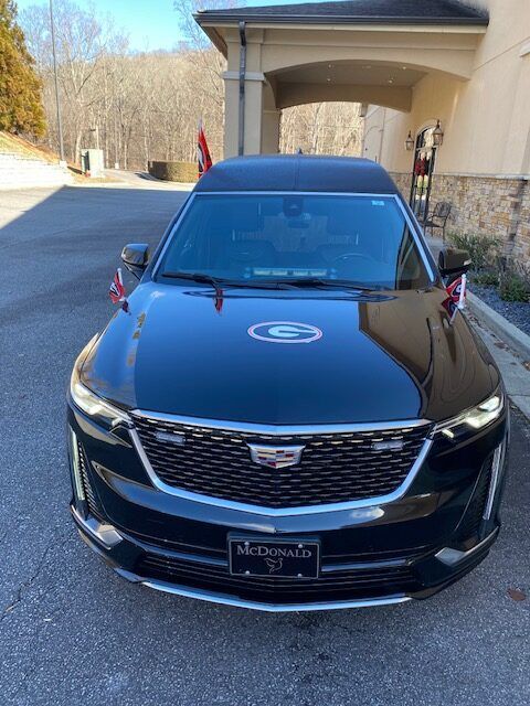 Black Cadillac sedan parked in a driveway under a covered entrance, front view
