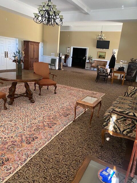 Spacious living room with patterned rugs, vintage furniture, chandelier, and TV on the far wall.