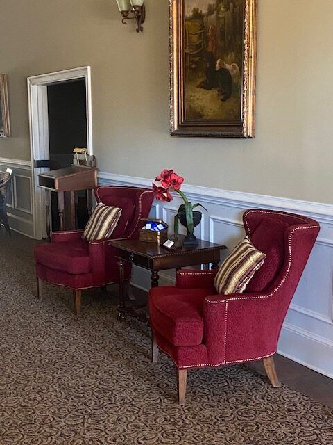Elegant seating area with two red armchairs, a side table with flowers, and a framed painting on the wall