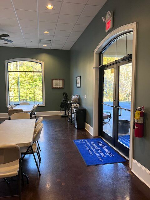 Meeting room with tables, chairs, arched windows, glass door, and a blue floor mat by the entrance
