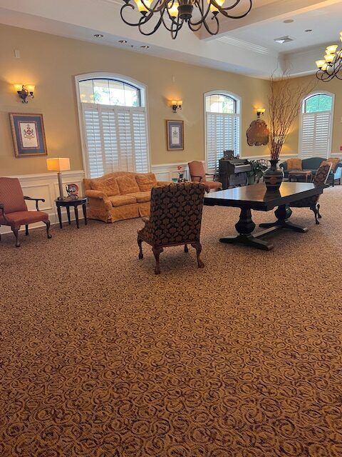 Elegant lounge with patterned carpet, sofas, armchairs, chandeliers, and large windows with shutters