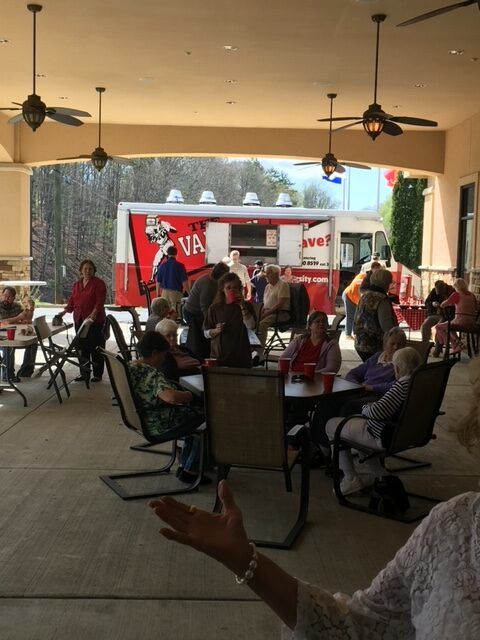 People gathered at outdoor café tables near a red food truck under a covered patio.