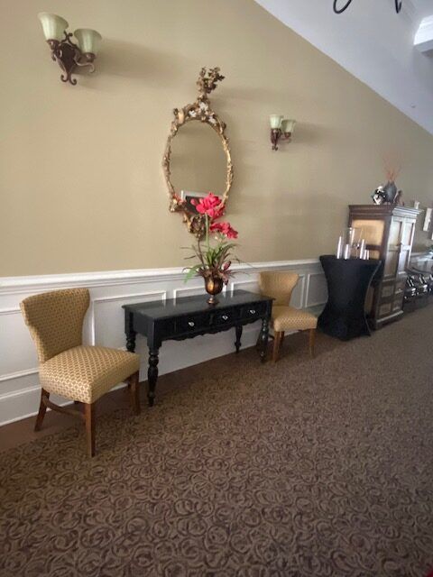 Decorative hallway with a black console table, mirror, flower vase, and two upholstered chairs on carpet.