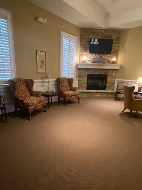 Cozy living room with two patterned chairs, fireplace, mounted TV, and tan carpet
