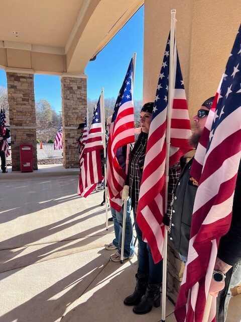 People holding American flags under a covered walkway in bright sunlight
