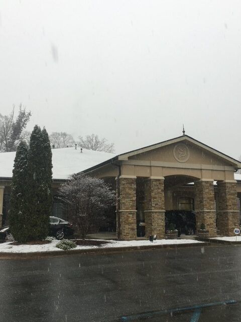 Snowy building entrance with brick columns and a dark road in front under an overcast sky