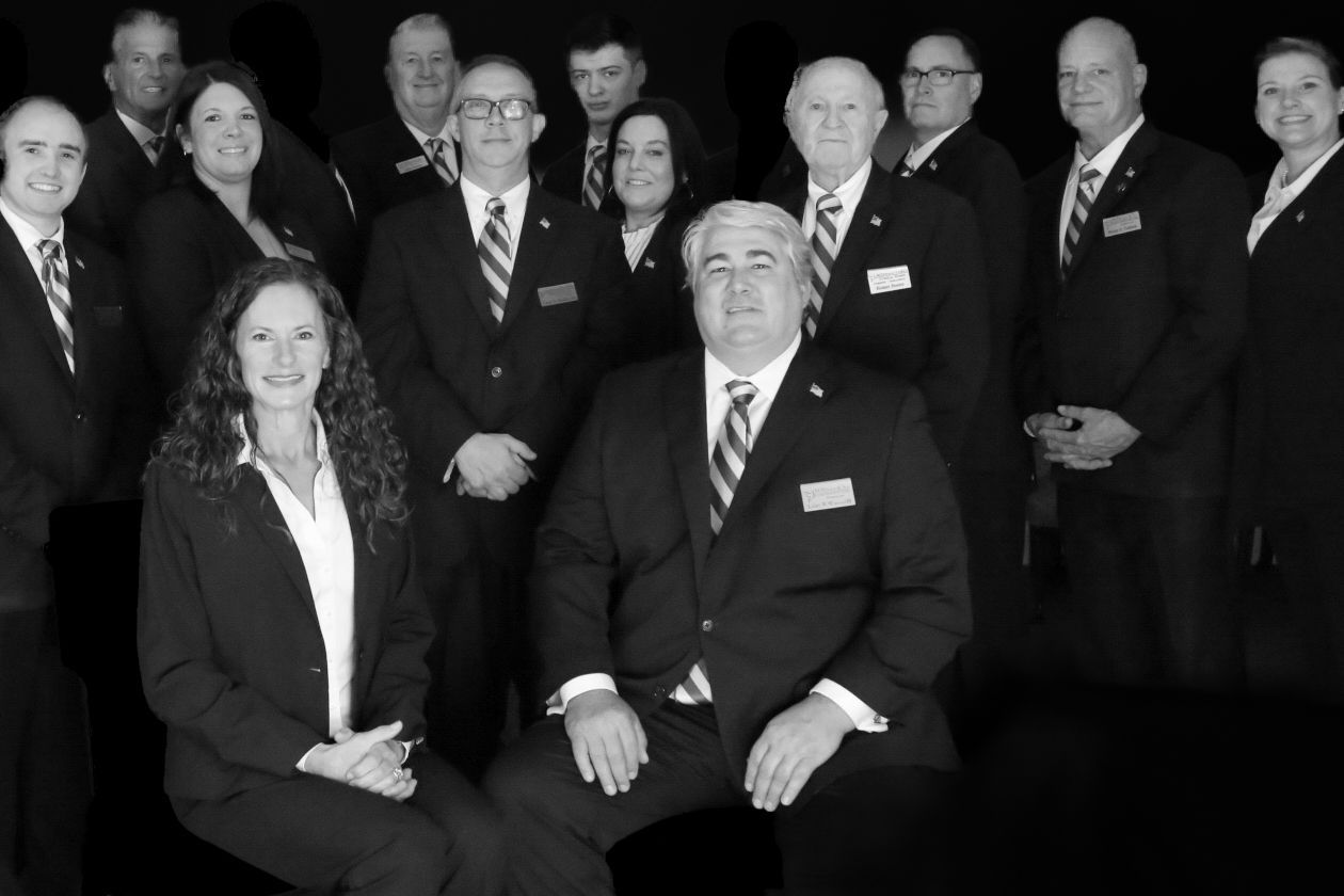 Group portrait of formally dressed people posing indoors, with a seated man and woman in front.