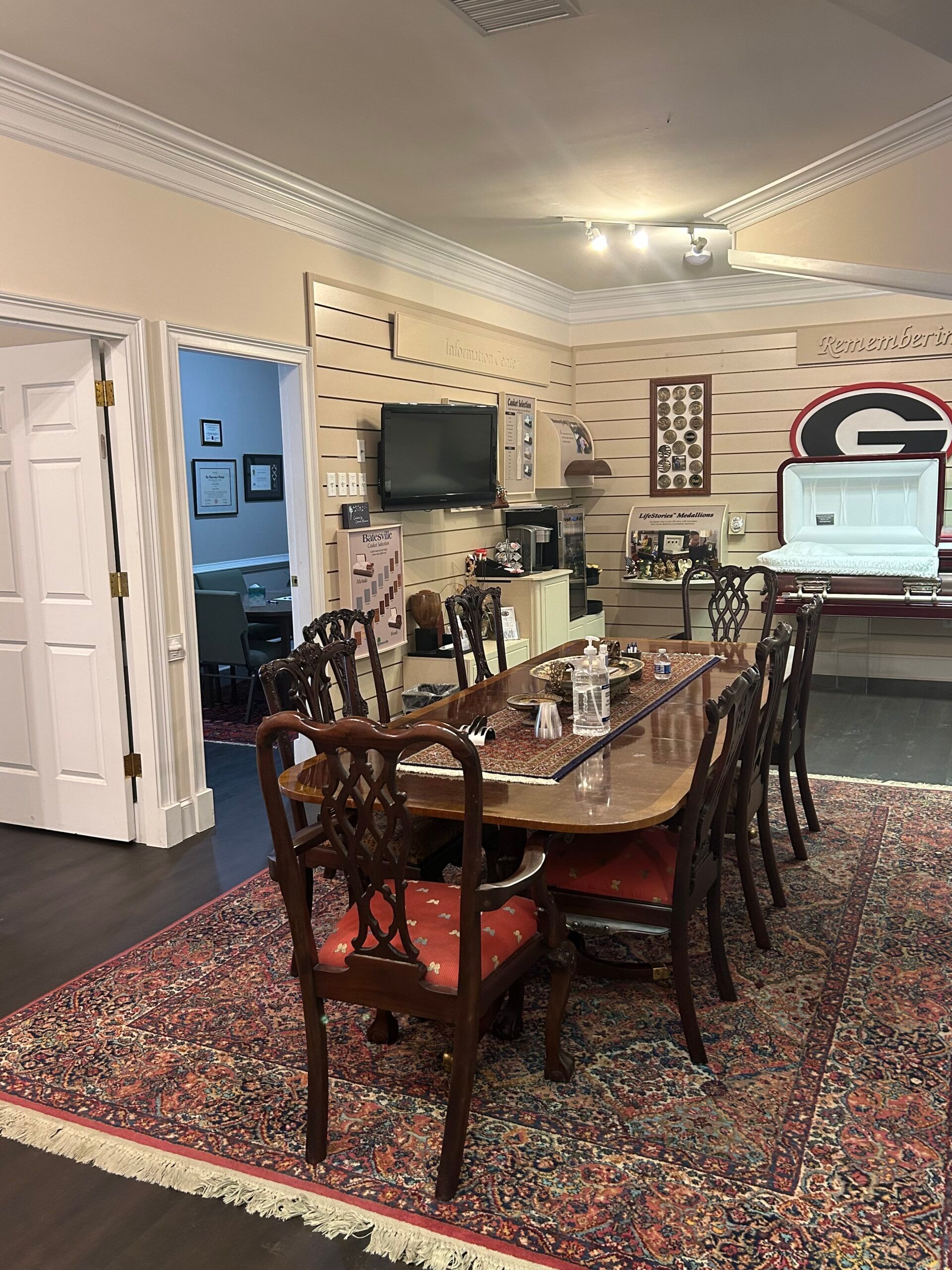 Conference room with long wooden table, patterned rug, wall-mounted TV, and Georgia Bulldogs logo decor.
