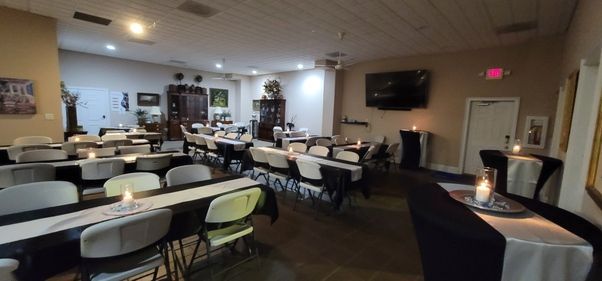 Empty banquet hall with round tables, white chairs, and a TV on the wall, lit by warm ceiling lights