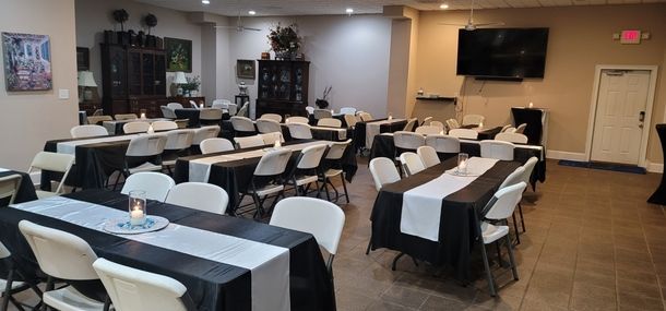 Dining room set for an event, with rows of white chairs and black tablecloths in a banquet hall.
