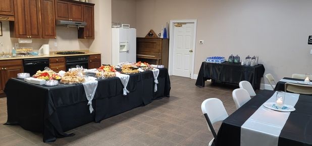 Buffet tables with food in a banquet hall beside white-clothed dining tables