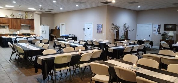 Empty conference room with rows of tables and chairs, kitchen area at left, and white doors at back