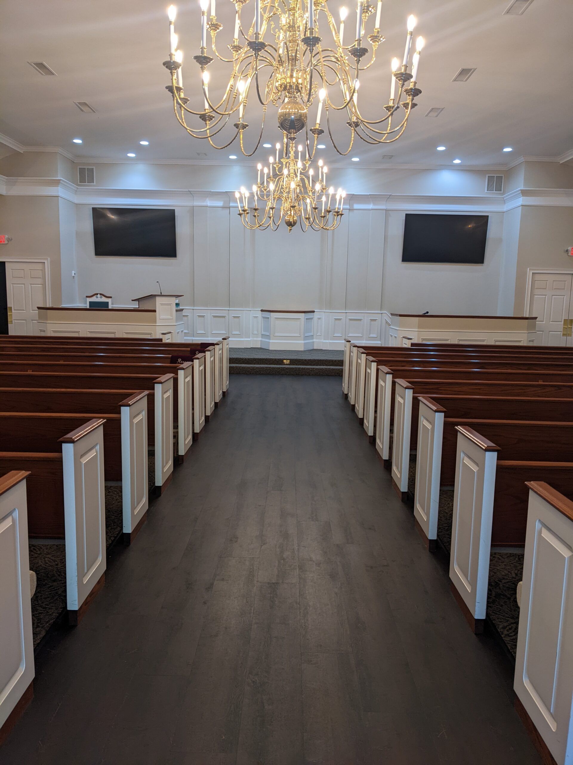Church sanctuary with wooden pews, chandeliers, and a central aisle facing the altar