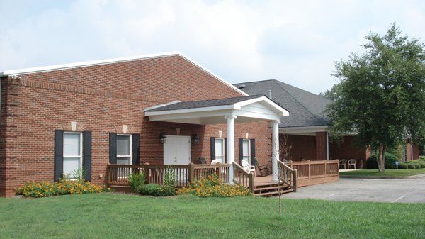Brick apartment building with a small covered porch, windows, and a grassy lawn under cloudy sky