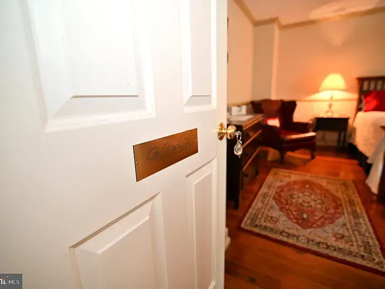 White door with bronze mail slot, partially open to bedroom with rug, bed, and lamp.