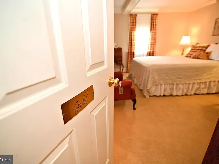 White door with "Carl" sign, leading into a peach-toned bedroom with bed and red chair.
