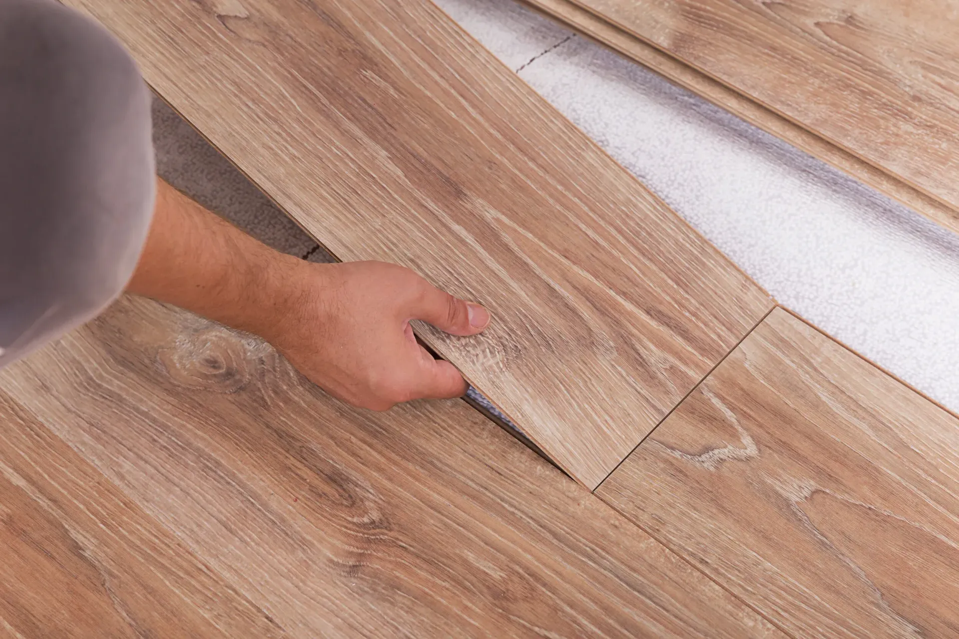Hand placing a wood-look floor plank into place on a light-colored subfloor