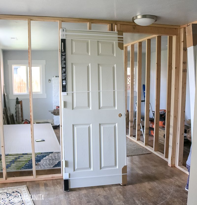 Interior room under renovation with exposed wall studs and a white door near a closet opening.
