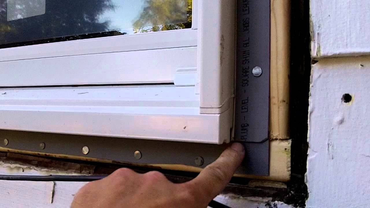 Hand pointing to the edge of a white window frame near a wall, showing a gap or installation seam.
